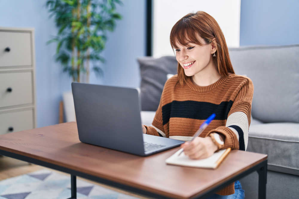 Young,Woman,Using,Laptop,Writing,On,Notebook,At,Home